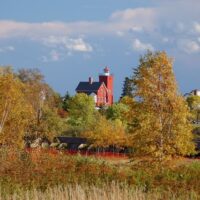 photo of the bright red brick Two Harbors lighthouse with fall foliage taken from a distance © Cindy Carlsson at ExplorationVacation.net