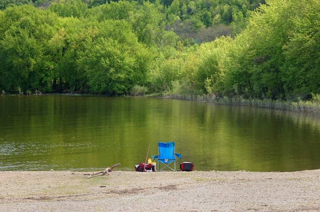 lawn chair, fishing poles, buckets, and other gear set up along the river bank