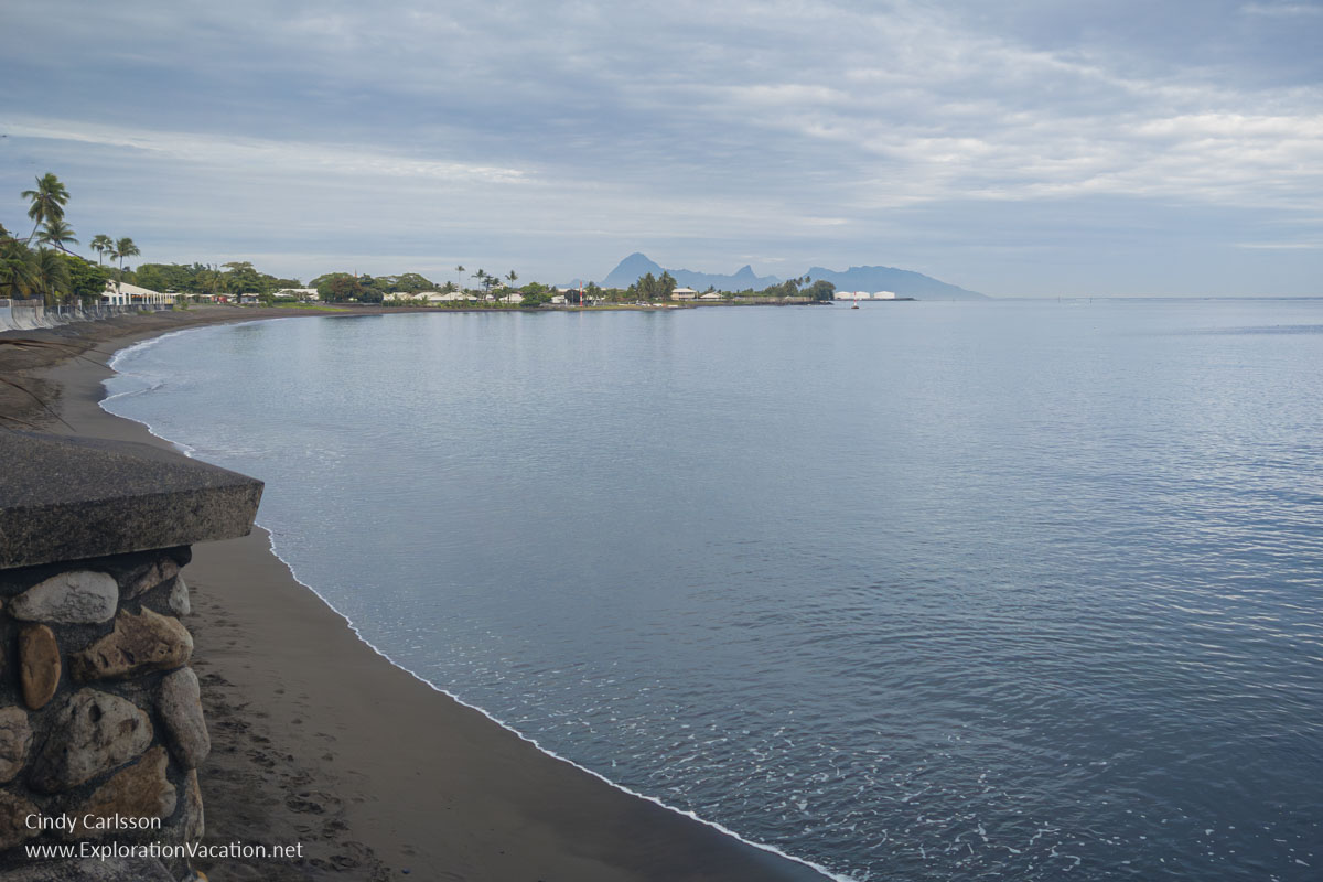 photo of the black sand beach with Mo'orea (and oil tanks) in the distance at the Royal Tahitian in Papeete, French Polynesia &copy; Cindy Carlsson at ExplorationVacation.net
