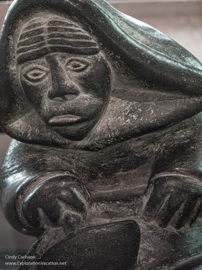 Face and hands of a stone carving of a woman with an ulu.