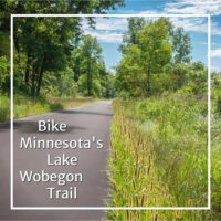 paved trail through woods and meadow with text "Bike Minnesota's Lake Wobegon Trail"