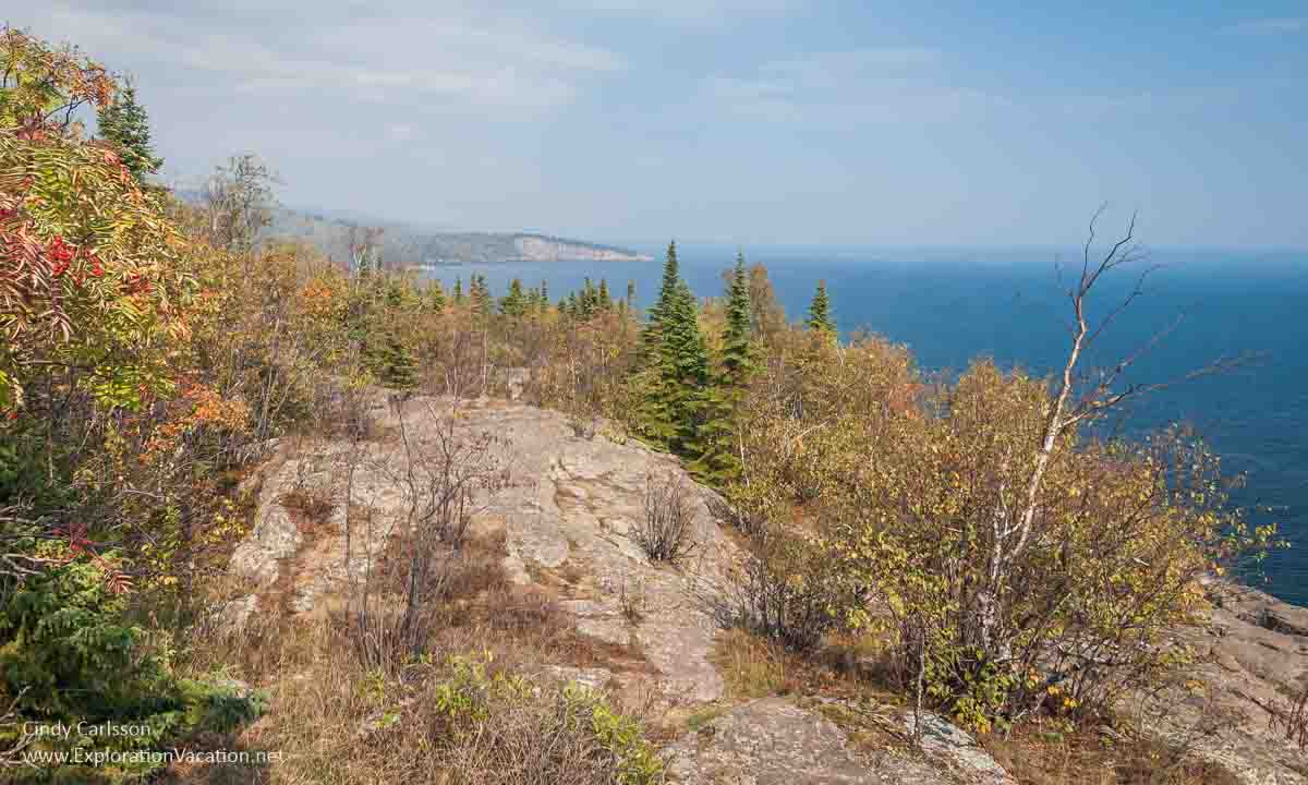 photo of Lake Superior and Shovel Point in the distance with rock and trees in the foreground taken from Palisade Head on Minnesota's North Shore © Cindy Carlsson at ExplorationVacation.net