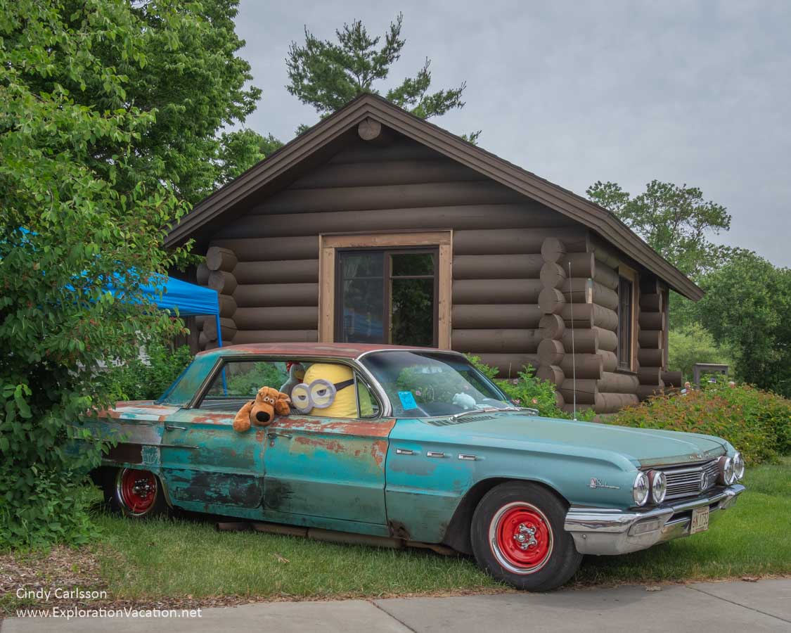 photo of a rusty vehicle with cartoon creatures parked by a log cabin at the 2019 Back to the 50s Weekend in Minnesota &copy; Cindy Carlsson ExplorationVacation.net