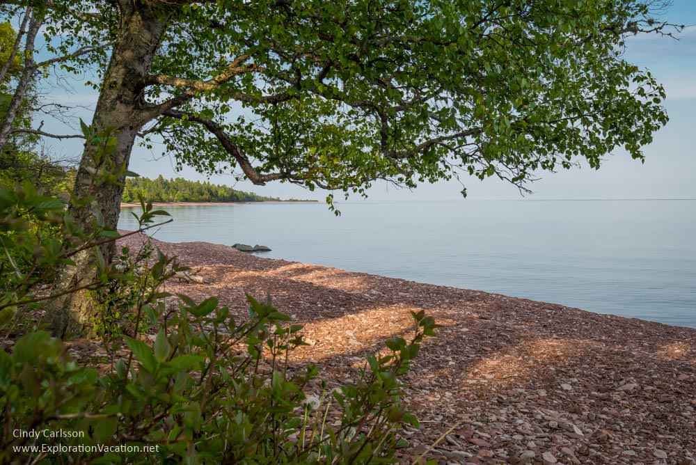 Photo of a tree over-hanging a gravel beach where the Kadunce River enters Lake Superior on Minnesota's North Shore © Cindy Carlsson at ExplorationVacation.net