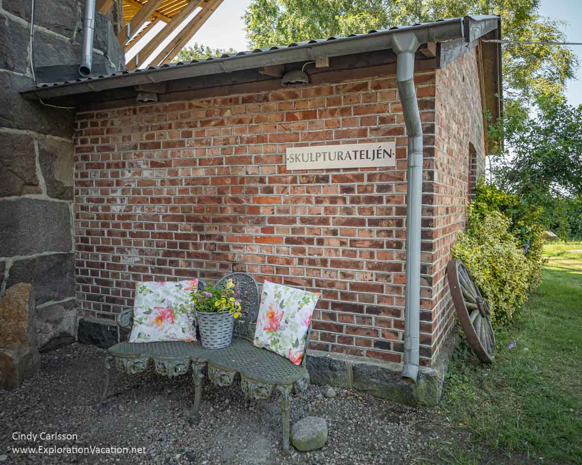 A small brick building with outdoor seating and a sign labeling this as a sculpture studio.