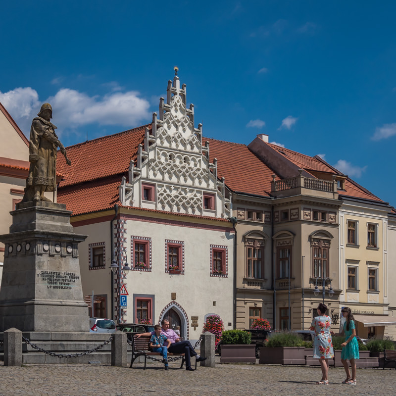 Statue and elaborately decorated buildings where people sit along the square
