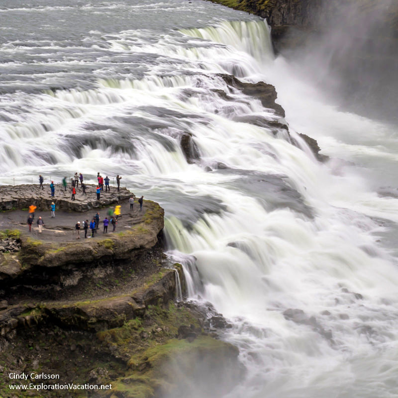 people on a rock outcrop overlooking a huge waterfall