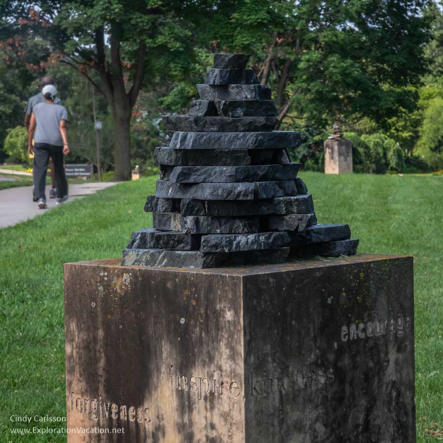 sculpture of a cairn on a stand with people in background 