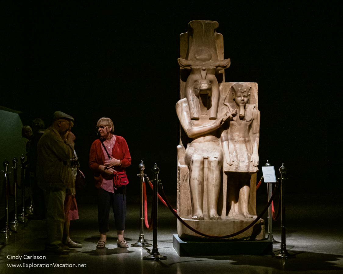large stone statue of a god and pharaoh with people standing near it