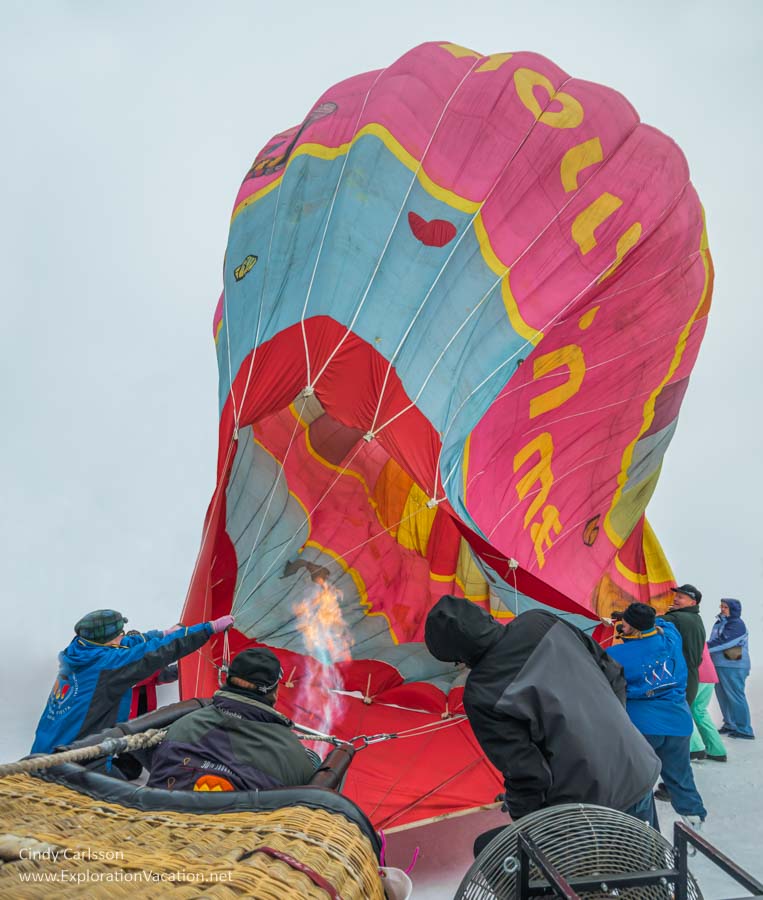 people struggle to inflate a balloon as the wind blows it around