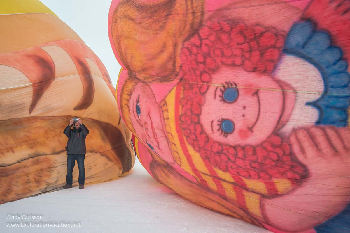 man taking pictures next to a partially-inflated hot air balloon with Raggedy Ann on the ground beside him