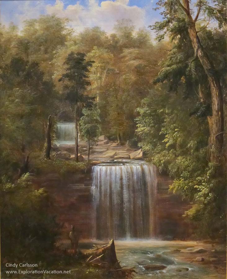Romanticized painting of a double waterfall with an American Indian