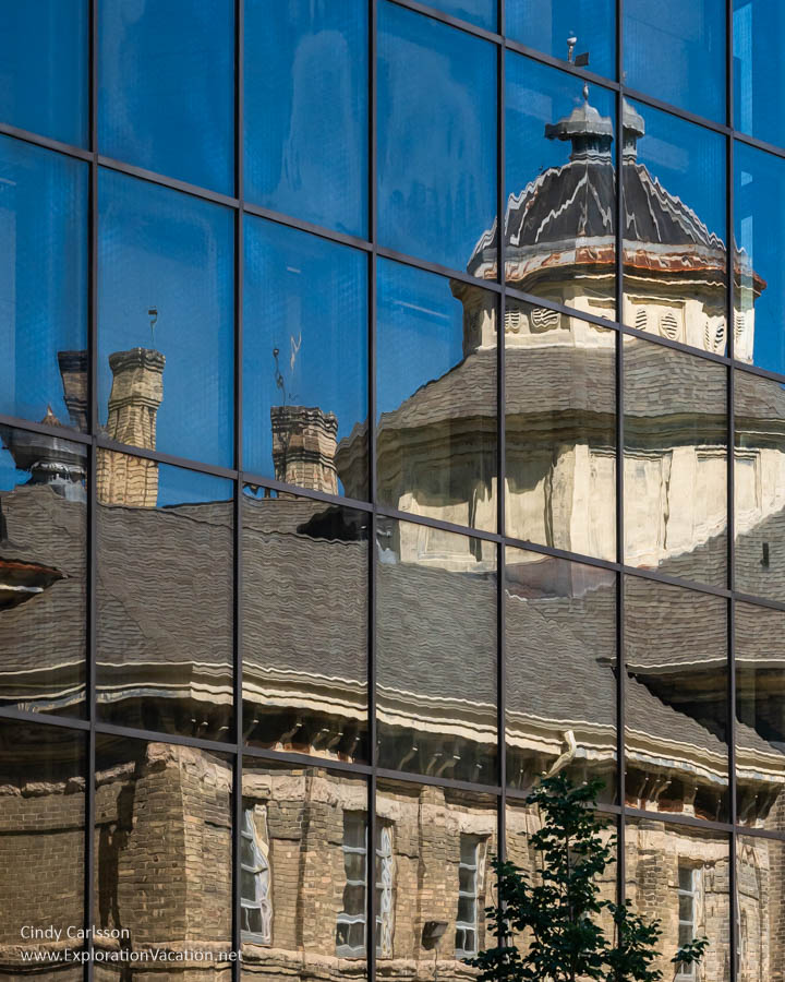 The Old Vaughan Street Jail cupola reflected in a contemporary glass-walled building on a sunny day.
