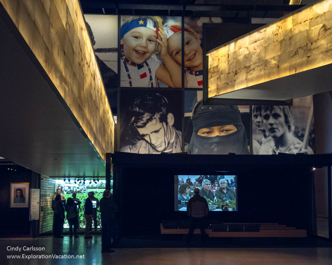 An exhibit area in the Canadian Museum for Human Rights with faces from different ethnic groups projected on a large wall and people standing below.
