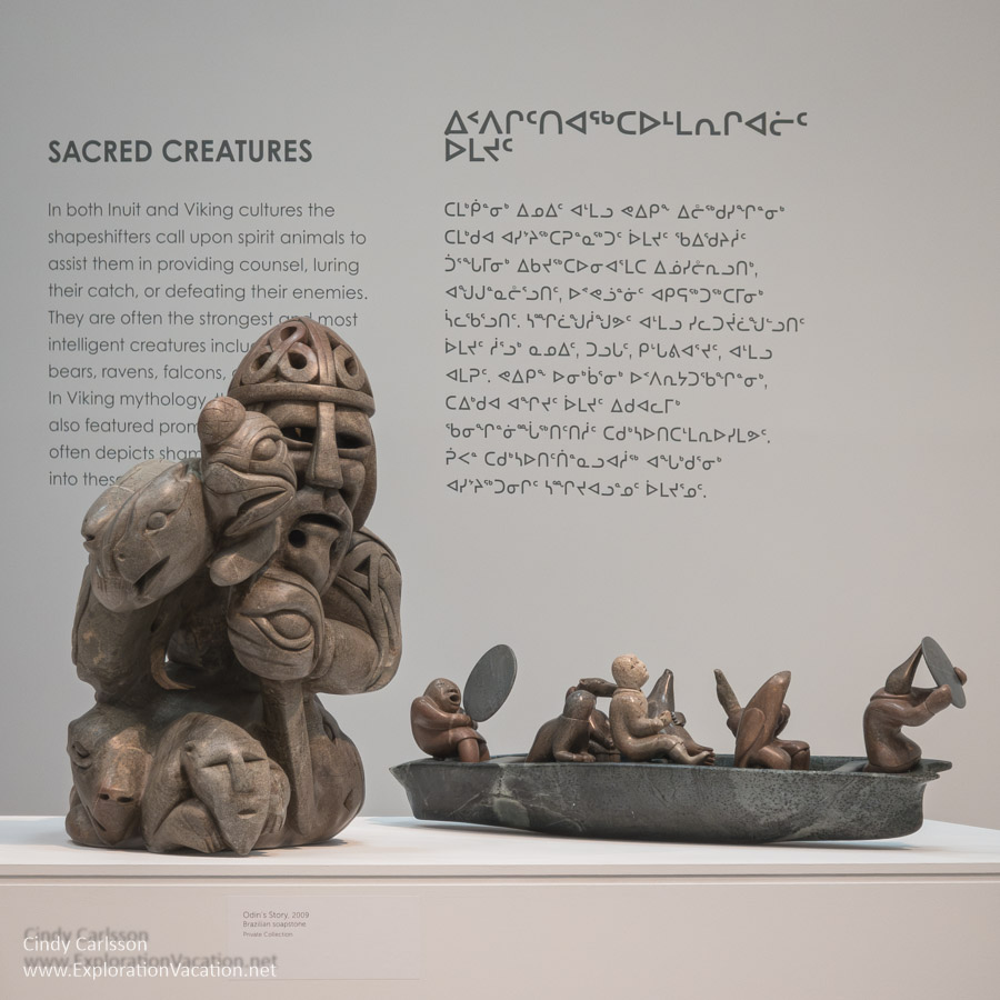 Stone carvings of a Viking and a boat with animal spirits by Abraham Anghik Ruben with informational signage on sacred creatures in the background.