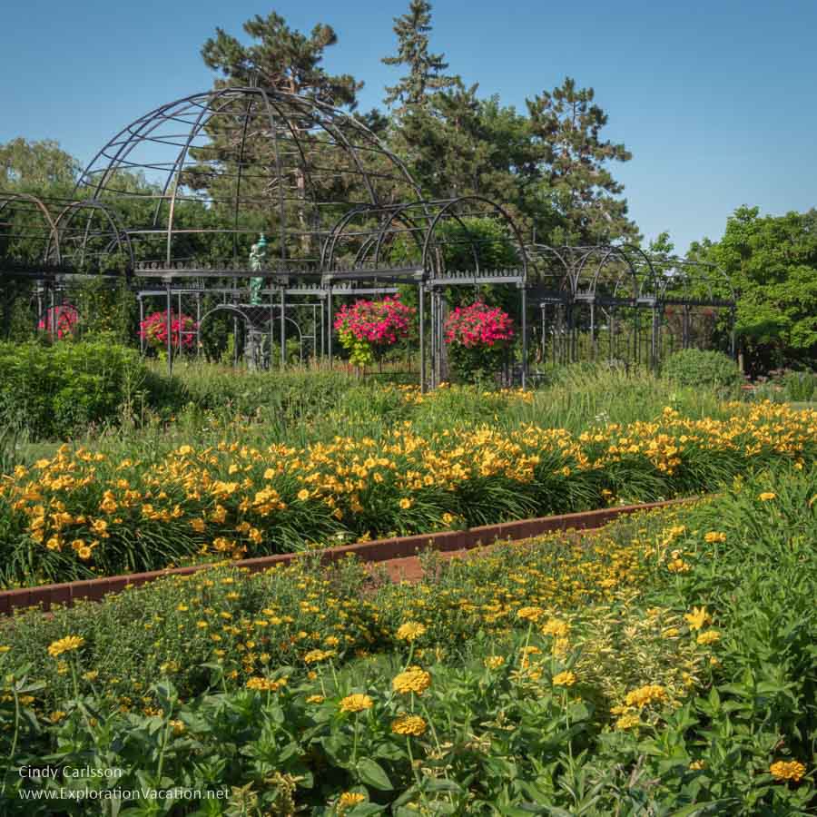 Walk-through metalwork forms a structure and serves as a trellis for surrounding flowers