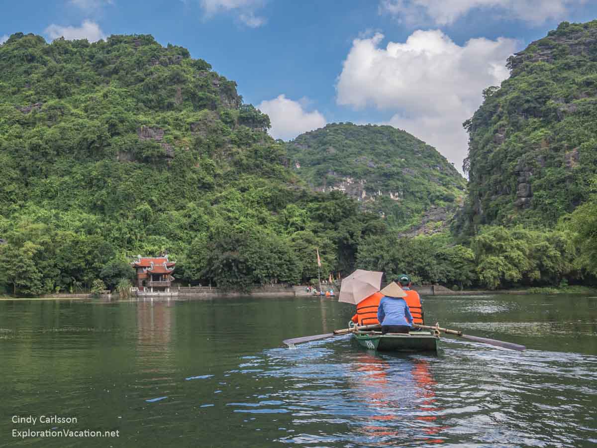 Photo of a flooded mountain valley with tourist rowboat and temple Trang An Vietnam - ExplorationVacation.net