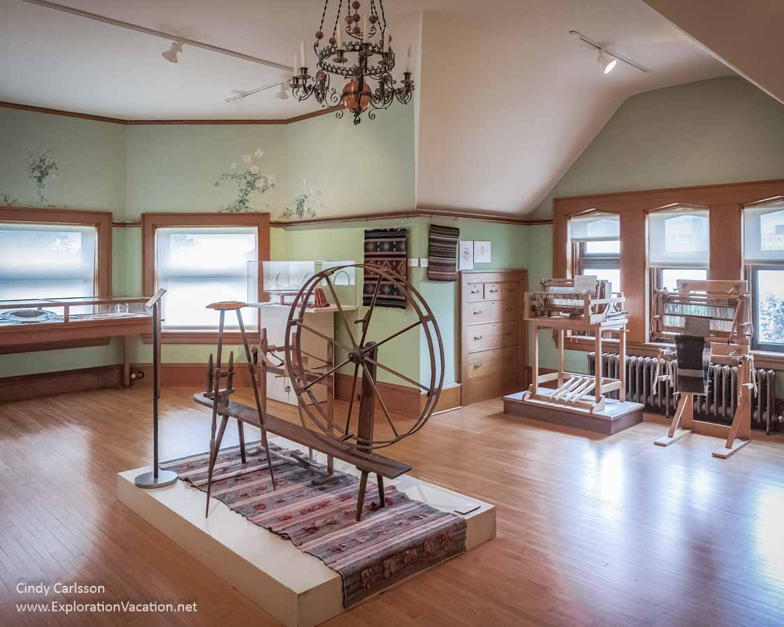 big open room with a spinning wheel, loom, and weavings 