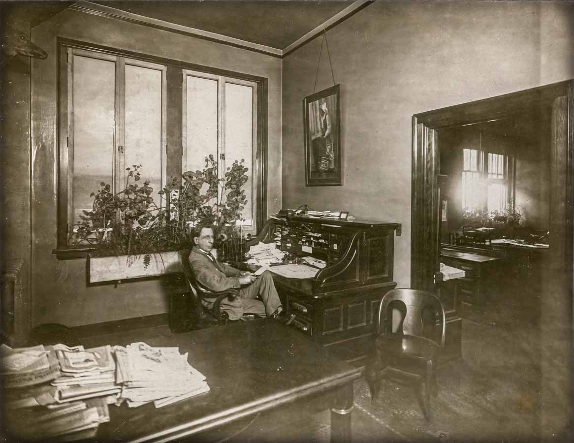 historic photo of a man sitting at a desk in a nice office