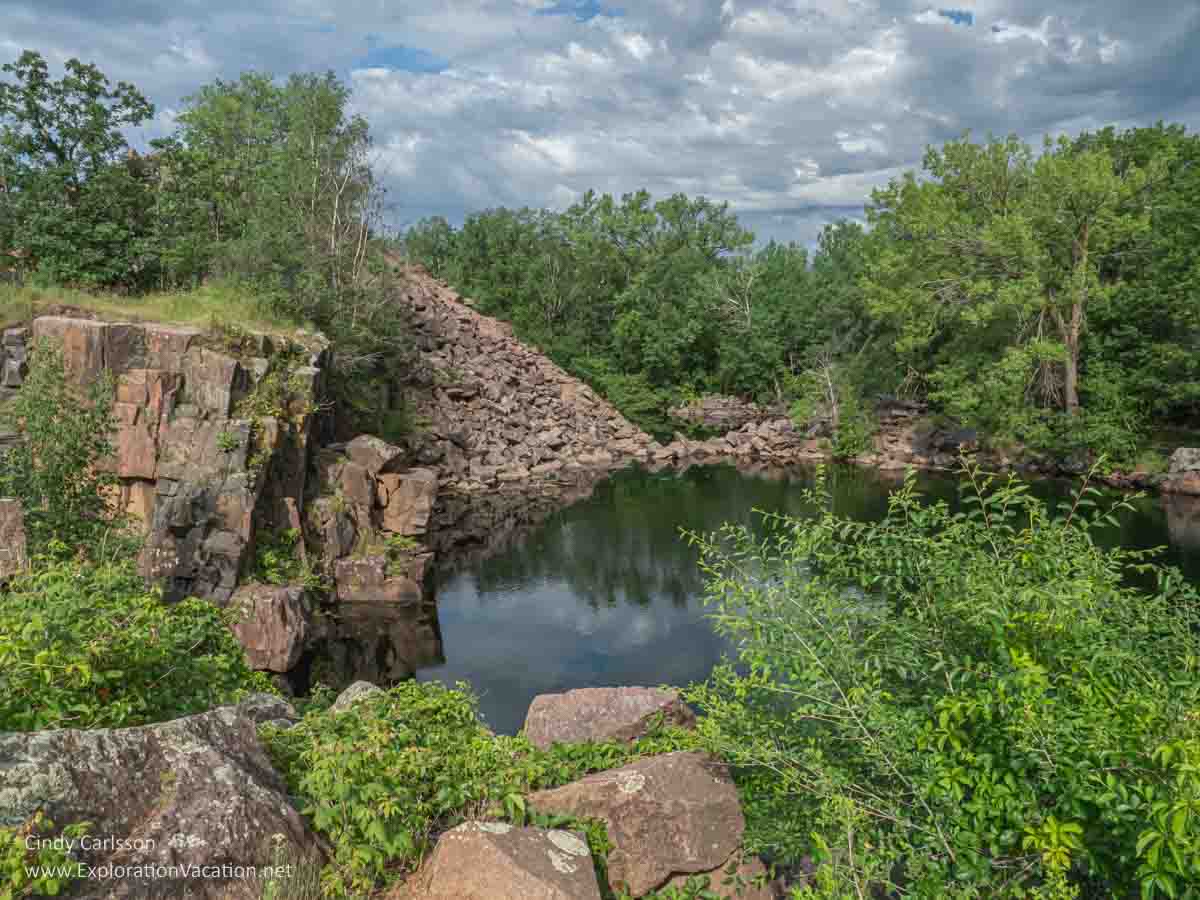Photo of landscape with woods, water-filled pits, and piles of waste stone at Quarry Park and Nature Preserve near St Cloud in central Minnesota. © Cindy Carlsson ExplorationVacation.net