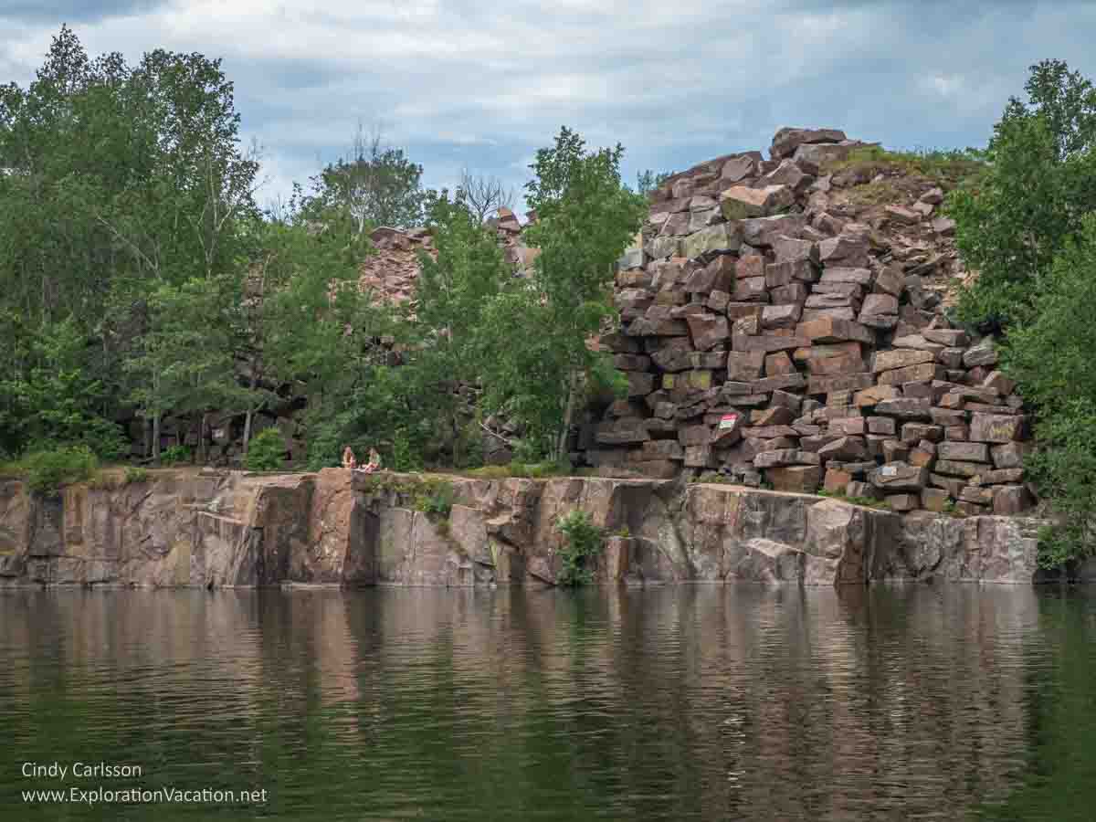 Photo of a water-filled quarry with a pile of stone behind it at Quarry Park and Nature Preserve near St Cloud Minnesota. Text and photos © Cindy Carlsson ExplorationVacation.net 