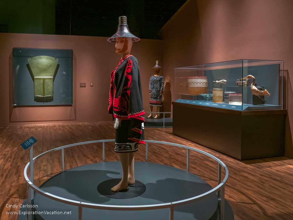 photo of a figure in traditional dress and items one would find in a clan house, but made of glass, by Tlingit artist Preston Singletary for "Raven and the Box of Daylight" at the National Museum of the American Indian Washington DC © Cindy Carlsson at ExplorationVacation.net
