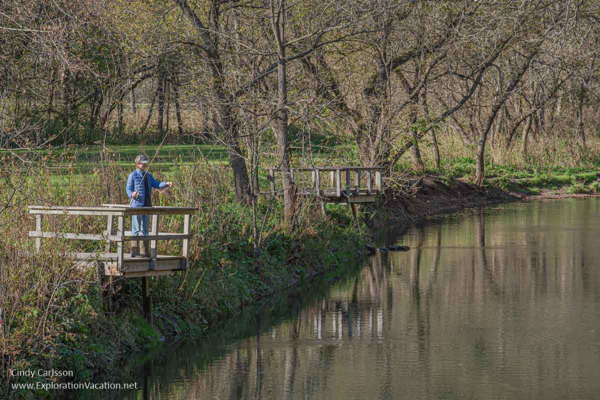 A person fishing in a still river from a small dock in fall.