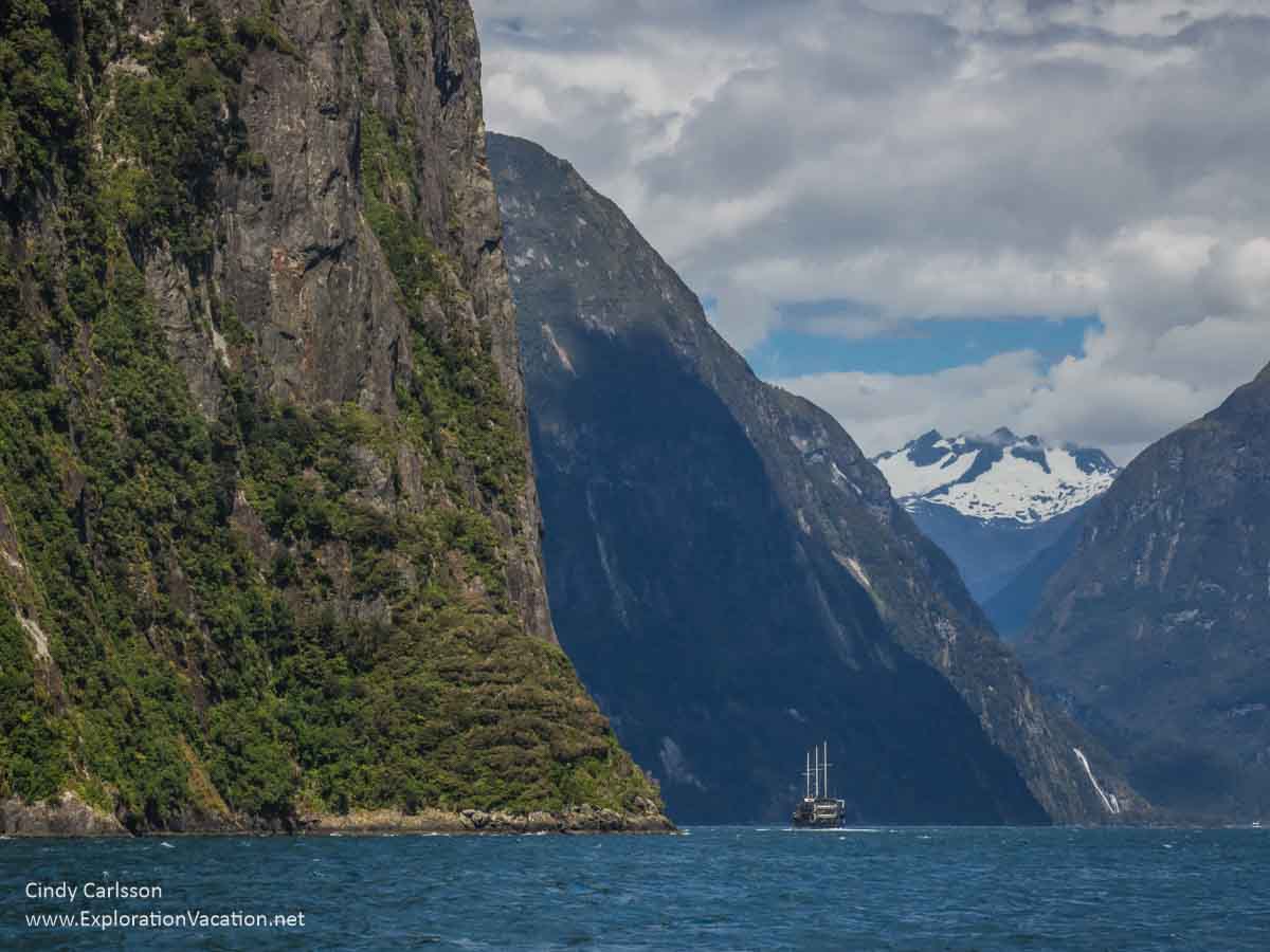 photo of a boat sailing beneath mountains on Milford Sound in Fiordlands National Park, part of the Te Wahipounamu South West New Zealand UNESCO World Heritage site &copy; Cindy Carlsson at ExplorationVacation.net 