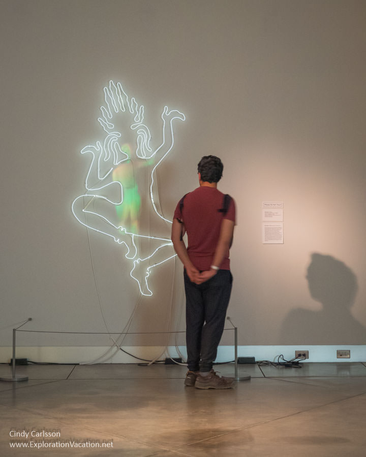 Photo of a man looking at &ldquo;As An Aspara,&rdquo; neon sculpture with digital projection by Daniella Thach in the exhibit &ldquo;She Bends&rdquo; at the Museum of Glass in Tacoma, Washington in July 2023 &copy; Cindy Carlsson at ExplorationVacation.net
