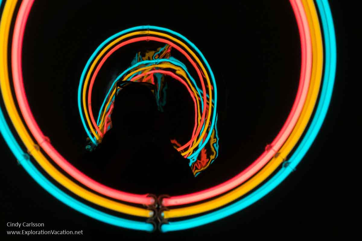 Photo of colorful repeating neon circles and the silhouette of a woman, part of the exhibit &ldquo;Room to Breathe&rdquo; in the &ldquo;She Bends&rdquo; exhibit at the Museum of Glass in Tacoma, Washington in July 2023 &copy; Cindy Carlsson at ExplorationVacation.net