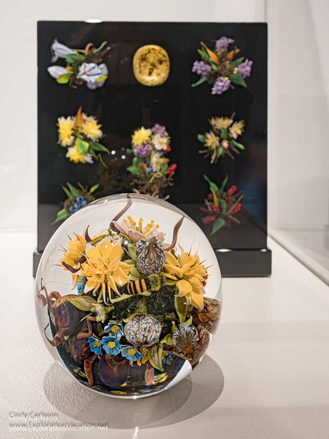Photo of an intricate botanical paperweight &ldquo;Fecundity Cluster Orb&rdquo; by Paul Stankard with a larger piece by Stankard in the background at the Museum of Glass in Tacoma, Washington &copy; Cindy Carlsson at ExplorationVacation.net