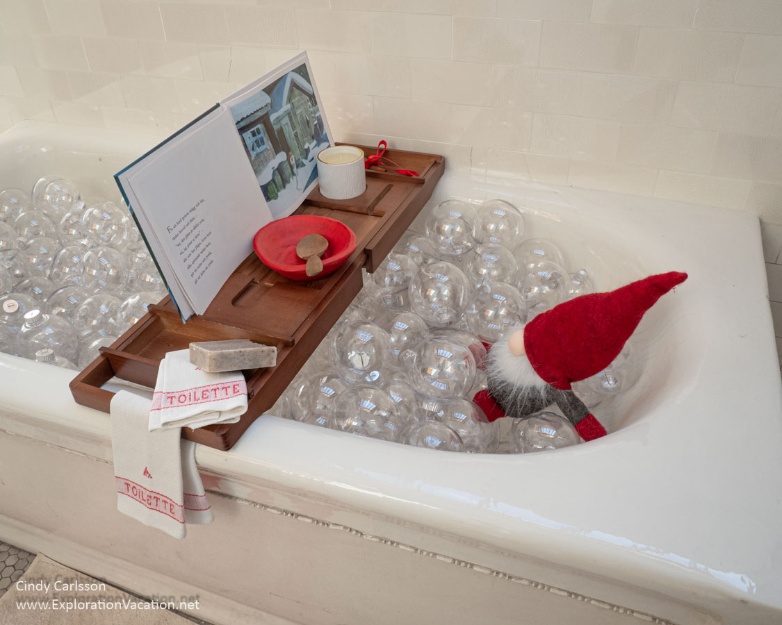 Photo of a Christmas elf (tomte) in a bathtub filled with glass &ldquo;bubbles&rdquo; reading a book set on a tray at the American Swedish Institute (ASI) Christmas display in Minneapolis, Minnesota &copy; Cindy Carlsson at ExplorationVacation.net