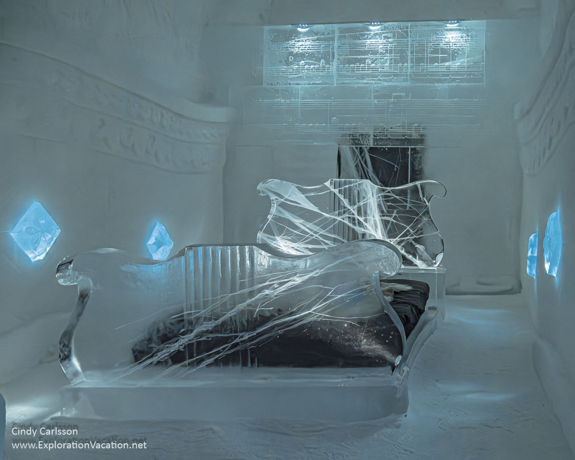 Photo of a carved ice bed with head and foot &ldquo;boards&rdquo; shaped like oversized music stands and a large music score (carved in ice) overhead in the Raindrop Prelude suite designed by Thomasz Czajkowski and Eryk Marks for Icehotel 365 in Jukkasj&auml;rvi, Swedish S&aacute;pmi (Lapland) &copy; Cindy Carlsson ExplorationVacation.net