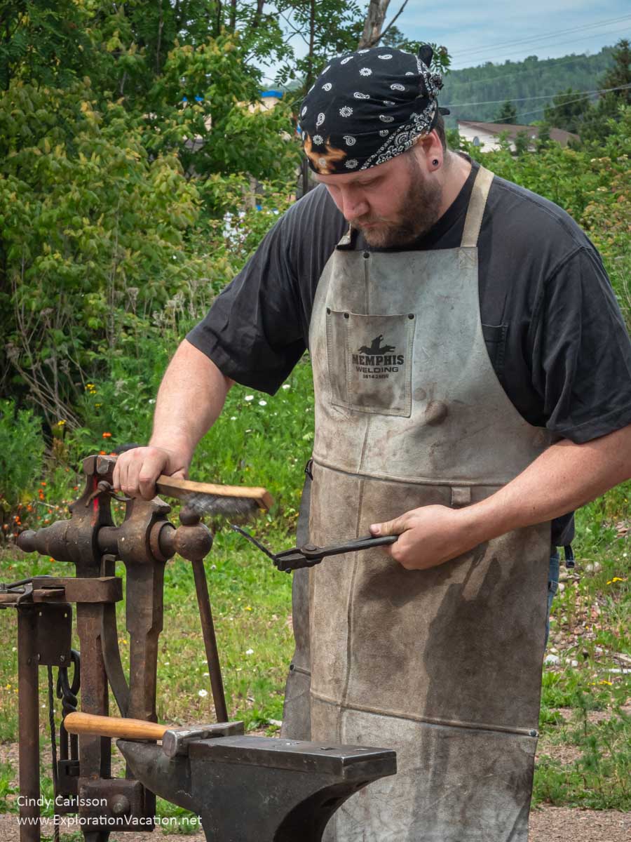 Photo of a young man shaping a piece of metal at a blacksmithing demonstration at the Bally Blacksmith Shop in Grand Marais, Minnesota &copy; Cindy Carlsson at ExplorationVacation.net
