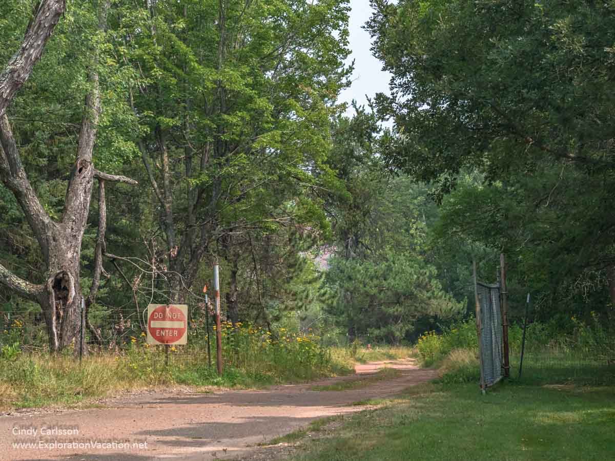 Photo of a do not enter sign by a dirt track through a gate in a fence in the forest at Hill Annex Mine State Park © Cindy Carlsson ExplorationVacation.net