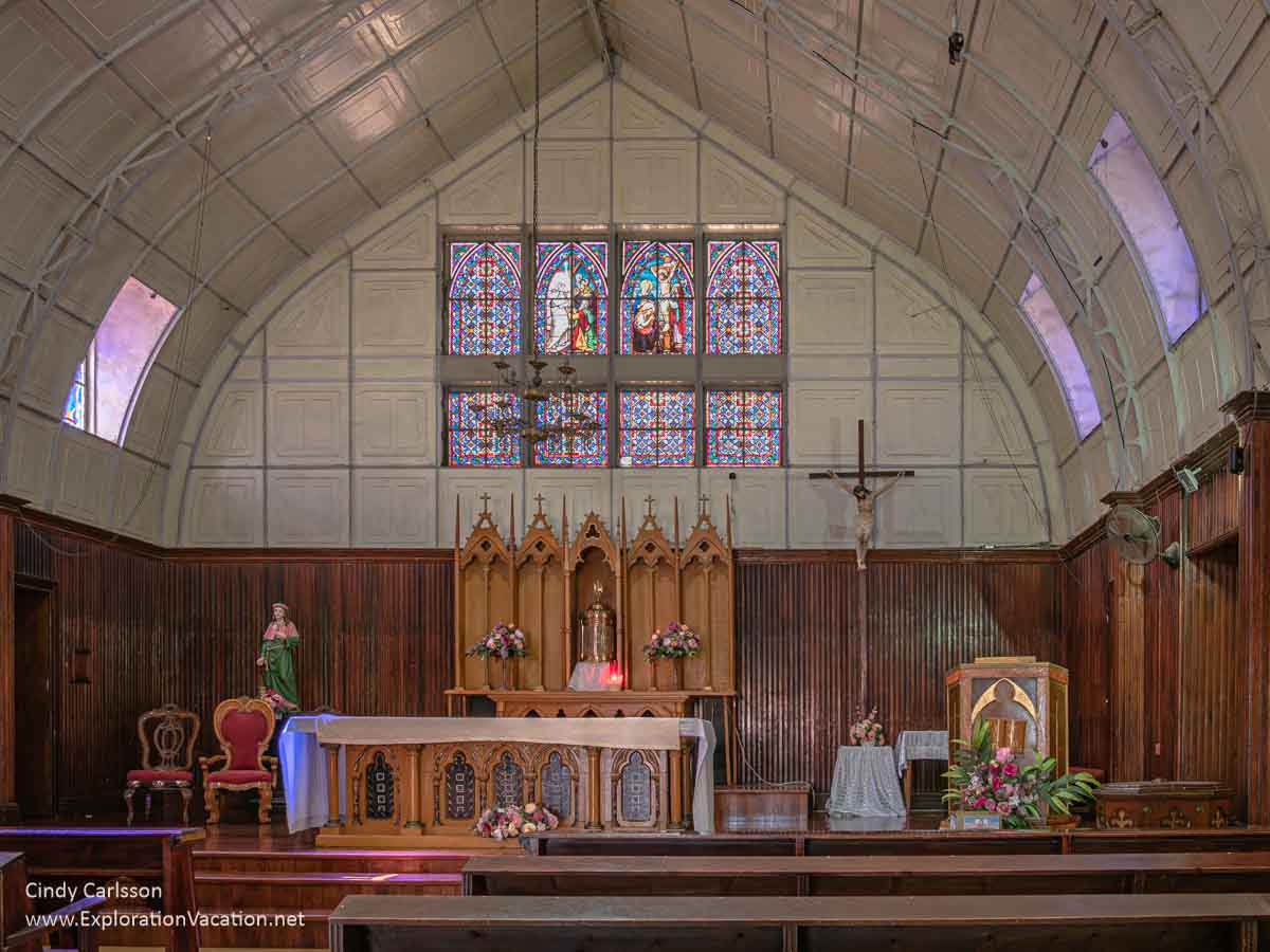 Wood altar, pulpit, cross, and other items in a simple white interior with large colored glass windows.