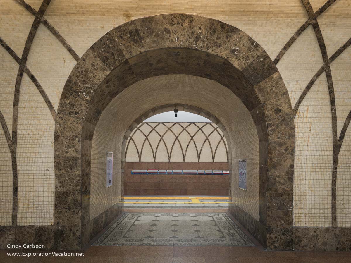 An archway with tiles that mimic the framework of a yurt in the background along the track in a metro station.