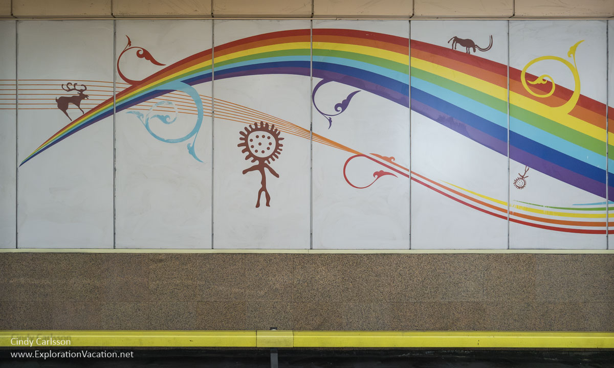 A painted mural of a rainbow with painted figures taken from ancient stone carvings.  