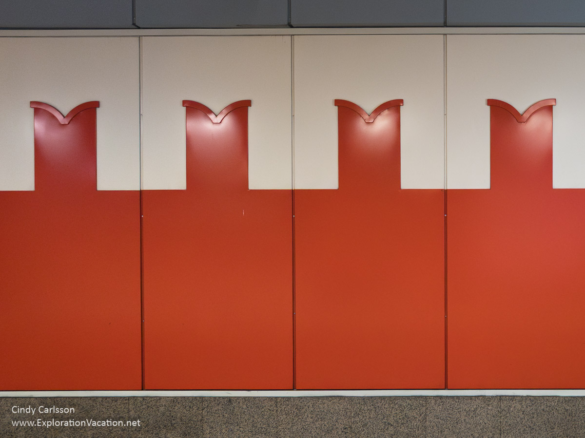 A red and white wall with a crenulated design that evokes the walls of the Kremlin in a metro station in Almaty.