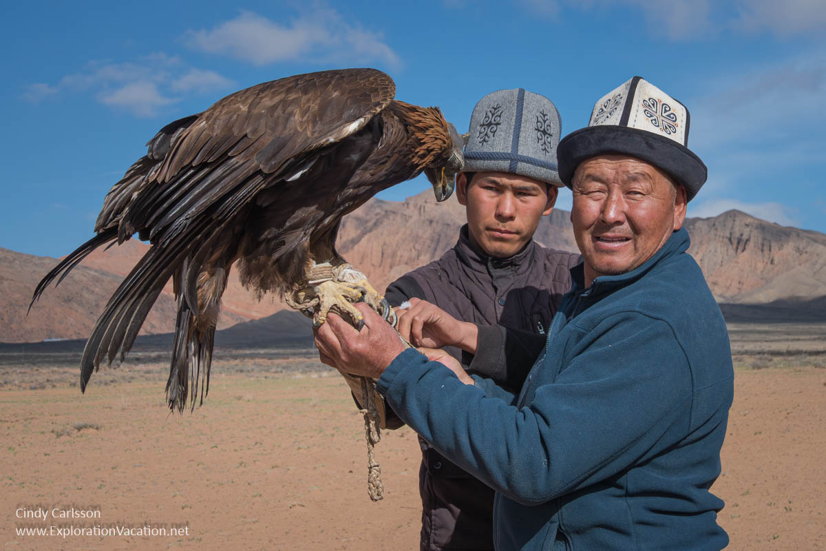 Two men in traditional hats holding a golden eagle.