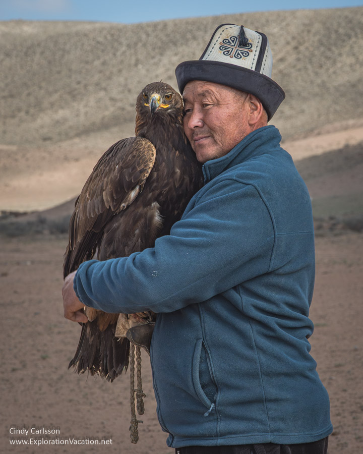 A man in a traditional hat hugging his golden eagle.
