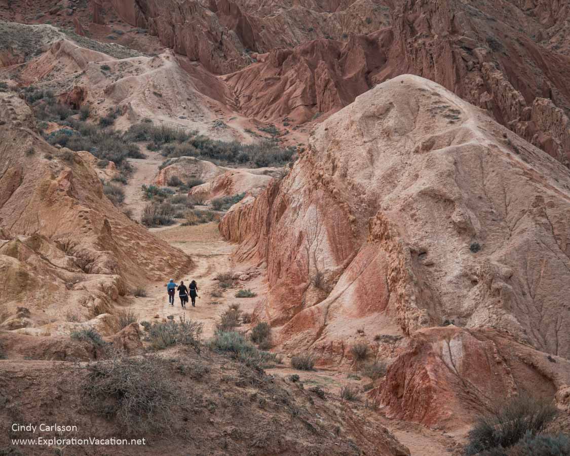 People walking through a colorful canyon, as viewed from higher up in the canyon. 