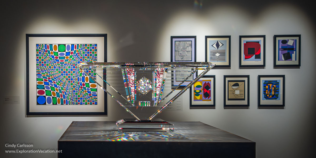 Bold serigraphs by Victor Vasarely behind a mostly clear glass sculpture by Jon Kuhn.