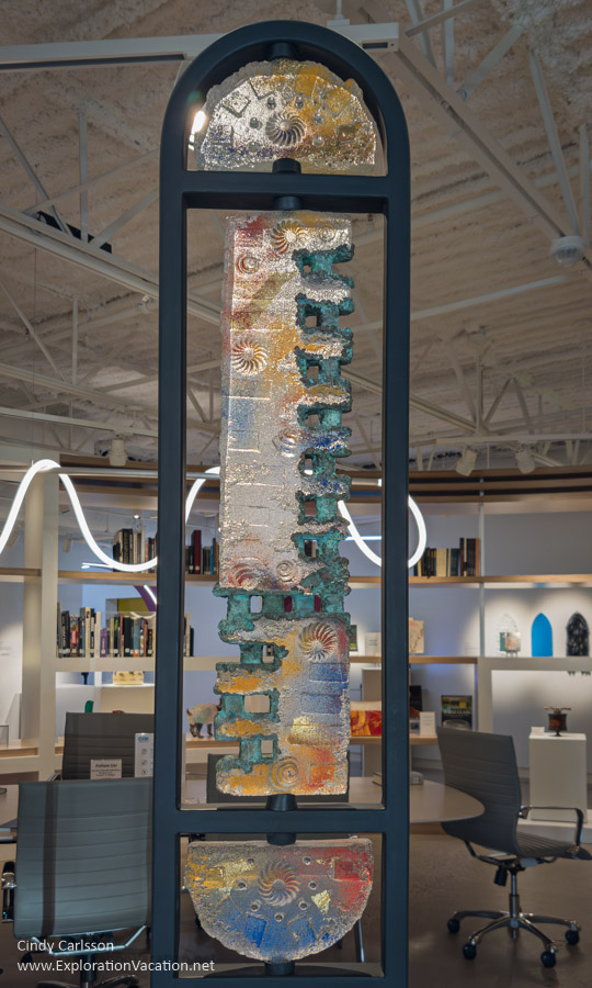 A large piece of glass art by Douglas Becker, with more art and library shelves visible in the background at the Cafesjian Art Trust Museum.
