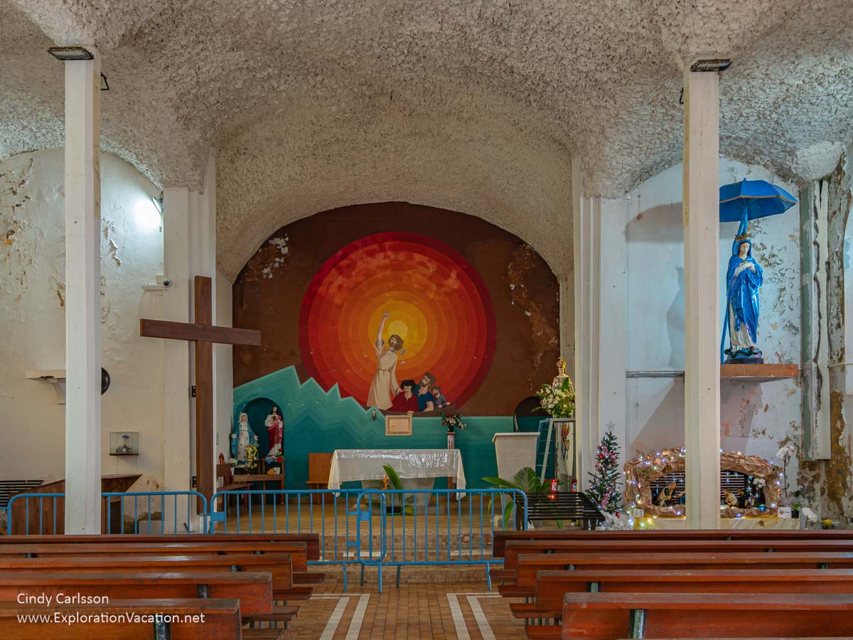 Notre-Dame des Laves church interior with a simple, bold mural, pews, and a sprayed ceiling. 