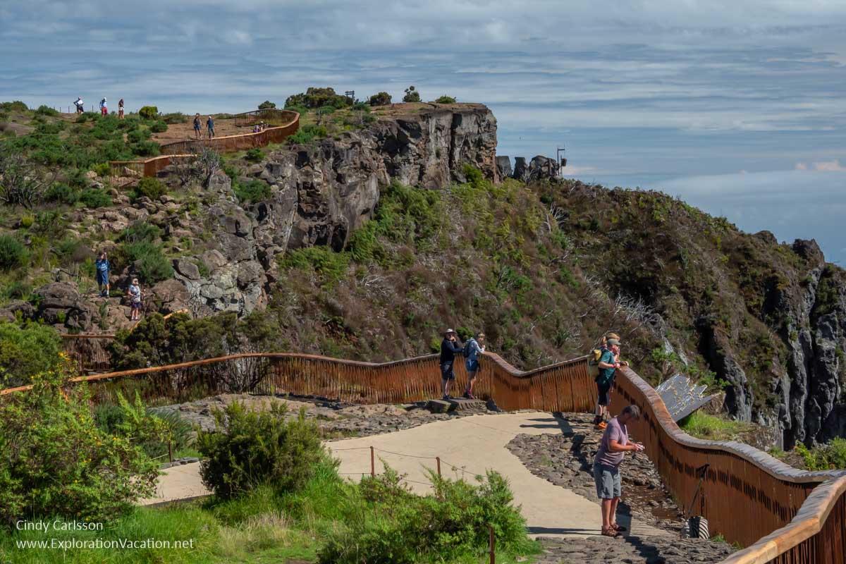 People along a fenced walkway that winds along the edge of a cliff.
