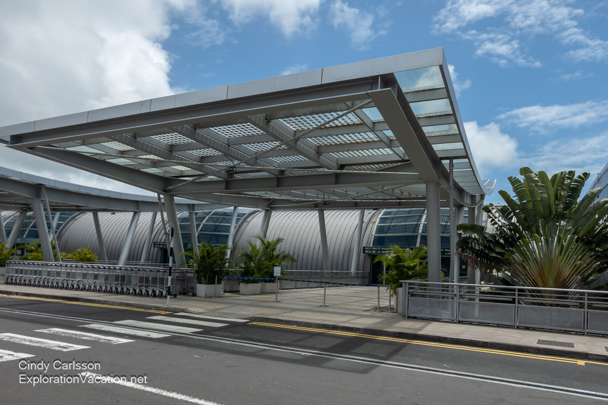 Exterior view of an entrance to the Mauritius airport with a floating glass canopy and rounded hall.