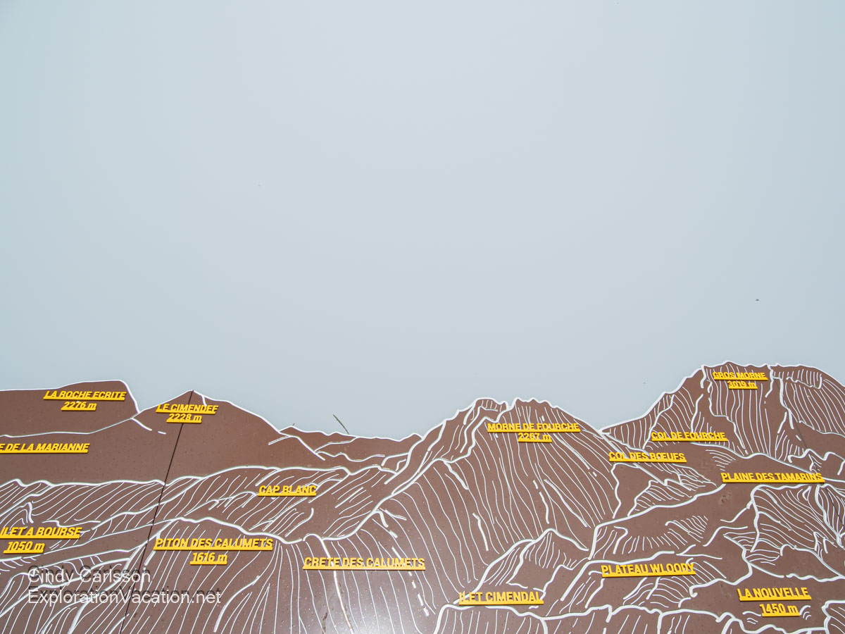 A sign identifying mountain peaks that are completely obscured by fog.