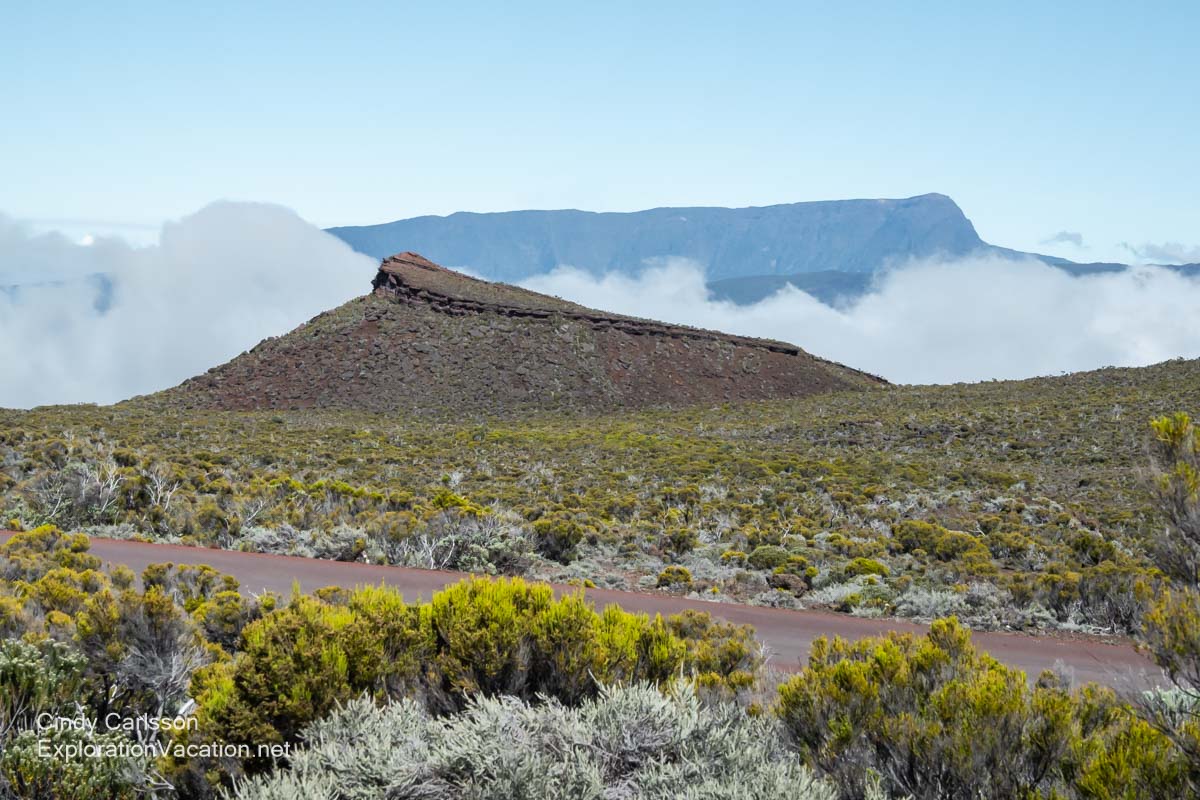 A volcanic ridge with mountains and fog behind it.