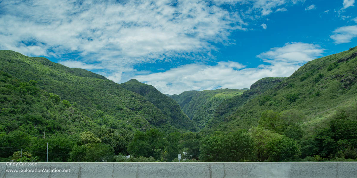 Large green hills along a highway with a few buildings partially visible at the base.